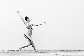 Image showing Fit sporty active girl in fashion sportswear doing yoga fitness exercise in front of gray wall, outdoor sports, urban style. Black and white photo.