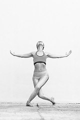 Image showing Fit sporty active girl in fashion sportswear doing yoga fitness exercise in front of gray wall, outdoor sports, urban style. Black and white photo.