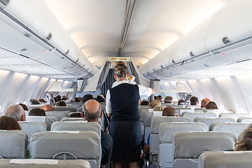 Image showing Interior of commercial airplane with stewardess serving passengers on seats during flight.