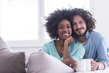 Image showing multiethnic couple sitting on sofa at home drinking coffe