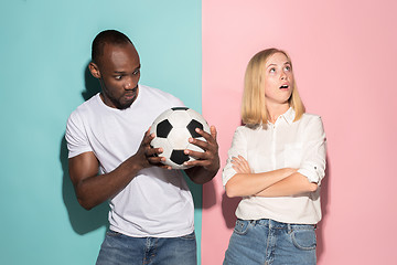 Image showing Closeup portrait of young couple, man, woman with football ball. They are serious, concerned on pink and blue background.