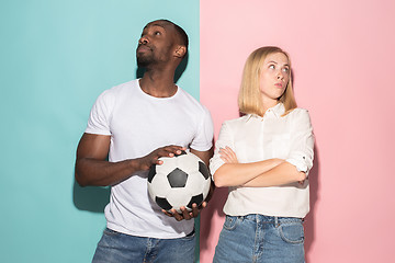 Image showing Closeup portrait of young couple, man, woman with football ball. They are serious, concerned on pink and blue background.