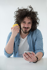 Image showing young man eating apple and using a mobile phone  at home