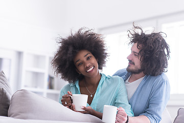 Image showing multiethnic couple sitting on sofa at home drinking coffe