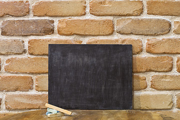 Image showing Blank clean blackboard an chalk on wooden table at brick wall. 