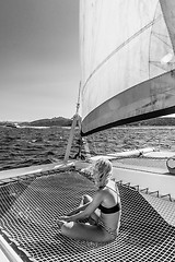 Image showing Beautiful woman relaxing on a summer sailing cruise, sitting and sunbathing in hammock of luxury catamaran sailing around Maddalena Archipelago, Sardinia, Italy.