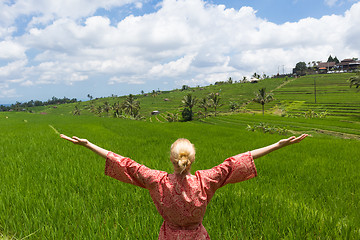 Image showing Relaxed fashionable caucasian woman wearing red asian style kimono, arms rised to sky, enjoying pure nature at beautiful green rice fields on Bali island