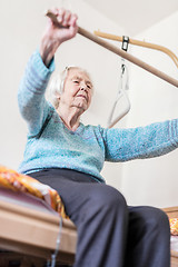 Image showing Elderly 96 years old woman exercising with a stick sitting on her bad.