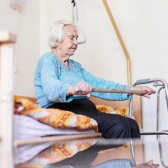 Image showing Elderly 96 years old woman exercising with a stick sitting on her bad.