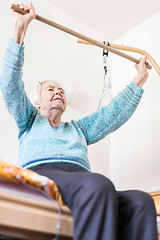 Image showing Elderly 96 years old woman exercising with a stick sitting on her bad.