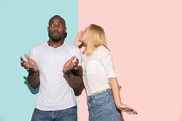 Image showing The young couple whispering a secret behind her hand over studio background