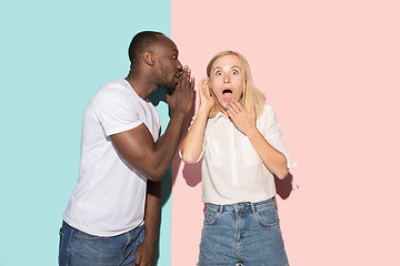 Image showing The young couple whispering a secret behind her hand over studio background