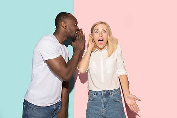 Image showing The young couple whispering a secret behind her hand over studio background