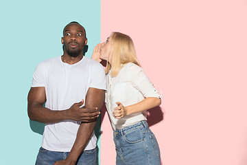 Image showing The young couple whispering a secret behind her hand over studio background