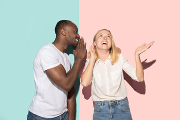 Image showing The young couple whispering a secret behind her hand over studio background