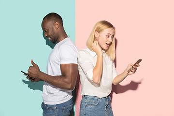 Image showing Mixed raced couple of students taking mobile phones. Caucasian girl and her African boyfriend posing at studio .