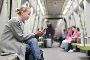 Image showing Beautiful blonde woman wearing winter coat reading on the phone while traveling by metro public transport.