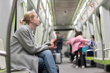 Image showing Beautiful blonde woman using smart phone while traveling by metro public transport.