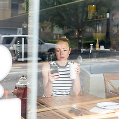 Image showing Thoughtful woman reading news on mobile phone during rest in coffee shop.