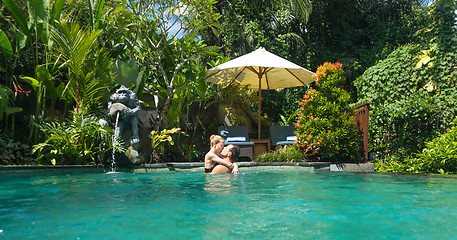 Image showing Happy couple kissing while relaxing in outdoor spa infinity swimming pool surrounded with lush tropical greenery of Ubud, Bali. Luxury spa and wellness vacation retreat concept