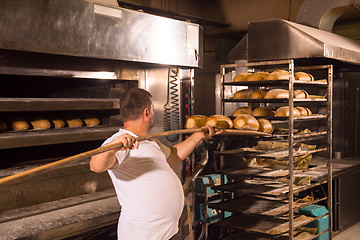 Image showing bakery worker taking out freshly baked breads