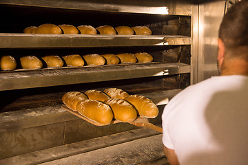 Image showing bakery worker taking out freshly baked breads