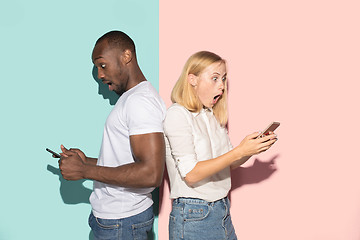 Image showing Mixed raced couple of students taking mobile phones. Caucasian girl and her African boyfriend posing at studio .