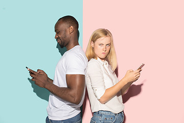 Image showing Mixed raced couple of students taking mobile phones. Caucasian girl and her African boyfriend posing at studio .