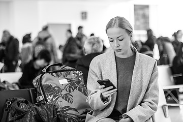 Image showing Female traveler reading on her cell phone while waiting to board a plane at departure gates at airport terminal.