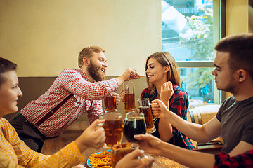 Image showing people, leisure, friendship and communication concept - happy friends drinking beer, talking and clinking glasses at bar or pub