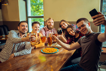 Image showing people, leisure, friendship and communication concept - happy friends drinking beer, talking and clinking glasses at bar or pub