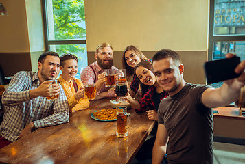 Image showing people, leisure, friendship and communication concept - happy friends drinking beer, talking and clinking glasses at bar or pub