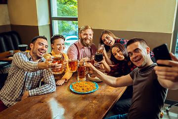 Image showing people, leisure, friendship and communication concept - happy friends drinking beer, talking and clinking glasses at bar or pub