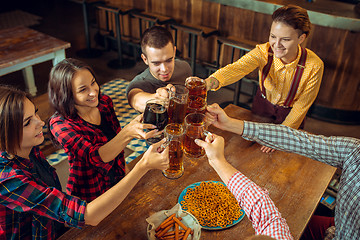 Image showing people, leisure, friendship and communication concept - happy friends drinking beer, talking and clinking glasses at bar or pub