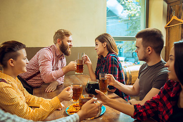 Image showing people, leisure, friendship and communication concept - happy friends drinking beer, talking and clinking glasses at bar or pub