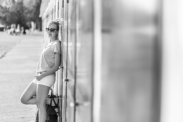 Image showing Blonde young female traveler wearing summer style clothing, leaning against retro blue beach dressing rooms at summer time vacation in Sistiana, Italy