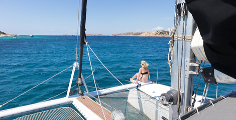 Image showing Woman relaxing on a summer sailing cruise, sitting on a luxury catamaran near picture perfect white sandy beach on Spargi island in Maddalena Archipelago, Sardinia, Italy.