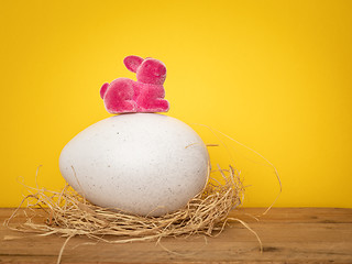 Image showing sweet Easter Bunny is sitting on a big egg yellow background