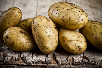 Image showing Newly harvested dirty potatoes heap on rustic wooden background.