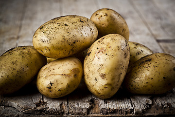 Image showing Newly harvested dirty potatoes heap on rustic wooden background.