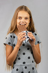 Image showing Ten-year girl bites chocolate and happily looks into the frame