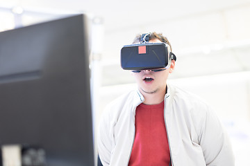 Image showing Young man wearing virtual reality headset and gesturing while sitting at his desk in creative office