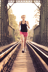 Image showing Active sporty woman running on railroad tracks.