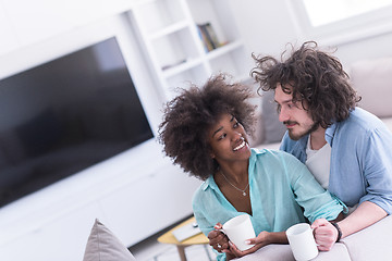 Image showing multiethnic couple sitting on sofa at home drinking coffe