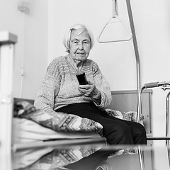 Image showing Elderly 96 years old woman operating TV or DVD with remote control in black and white.