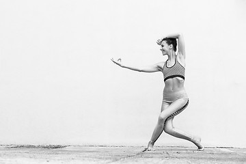 Image showing Fit sporty active girl in fashion sportswear doing yoga fitness exercise in front of gray wall, outdoor sports, urban style. Black and white photo.