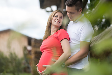 Image showing Young happy pregnant couple hugging at countryside by hayrack.