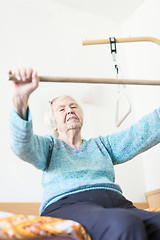 Image showing Elderly 96 years old woman exercising with a stick sitting on her bad.