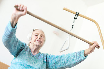 Image showing Elderly 96 years old woman exercising with a stick sitting on her bad.