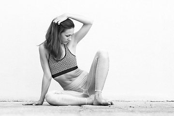 Image showing Fit sporty active girl in fashion sportswear sitting on the floor in front of gray wall. Black and white photo.